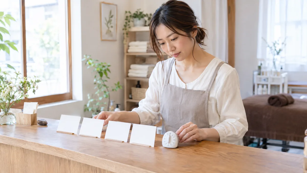 サロンの受付台で、店主が施術メニューのカードを並べ替えながら所要時間を見直している様子