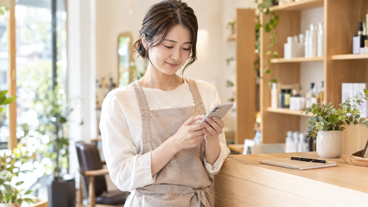 開業したばかりの小さな店で、オーナーがスマホの予約ページを確認している様子